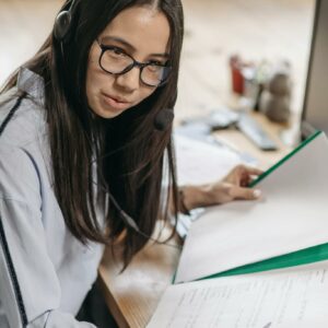 Woman in an office setting wearing a headset, reviewing documents seriously.